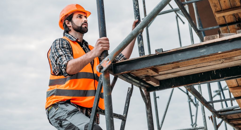 bearded builder climbing on scaffolding at construction site