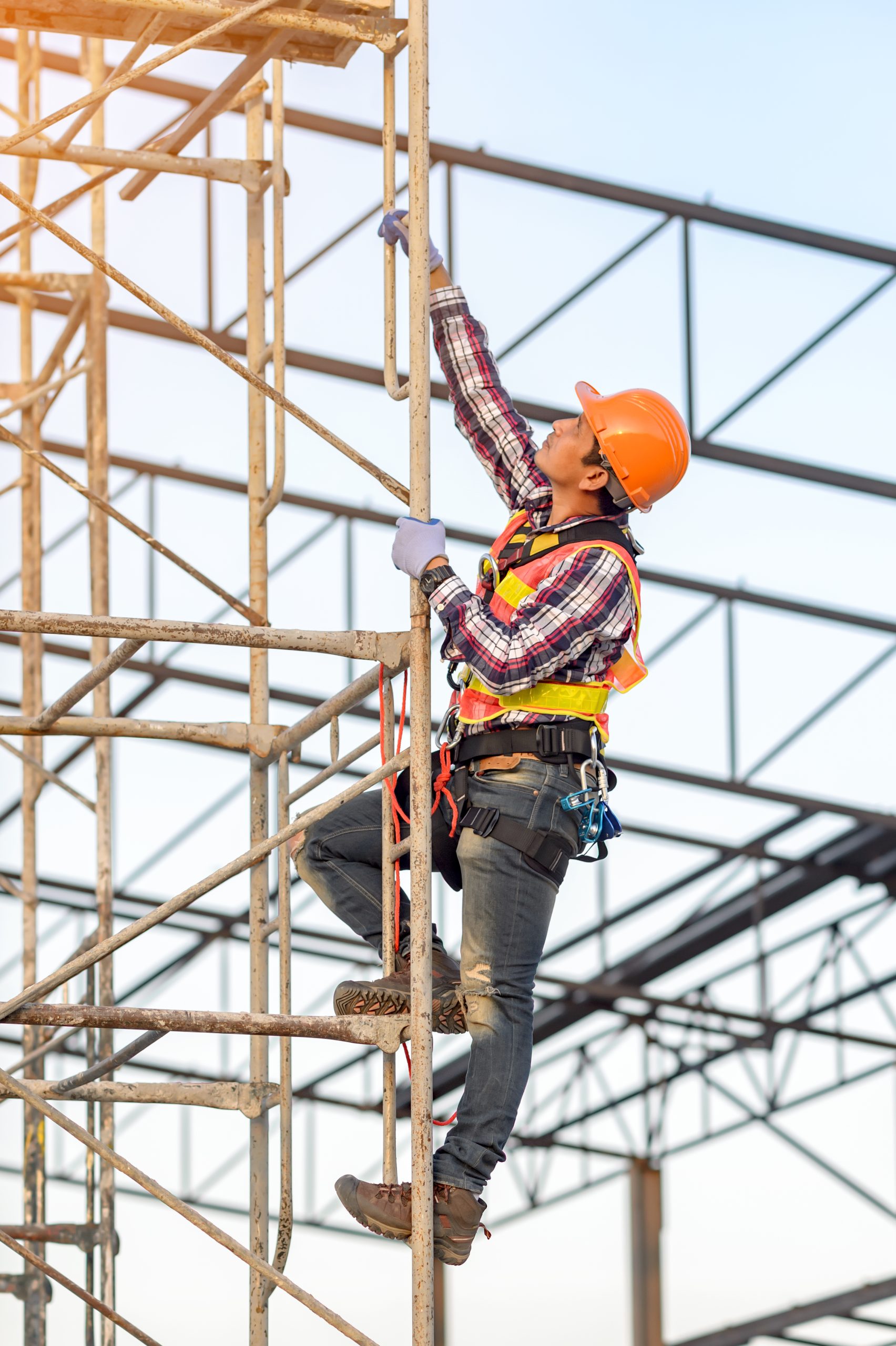 Trabajador equipado con arnés y casco de seguridad ascendiendo por una estructura de andamios